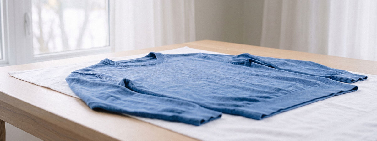 Una maglia blu tinta in capo ad asciugare in piano su un asciugamano vicino a una finestra